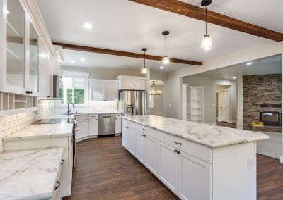A white kitchen with wooden beams and marble counter tops.