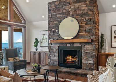 A living room with a stone fireplace and ceiling fan.