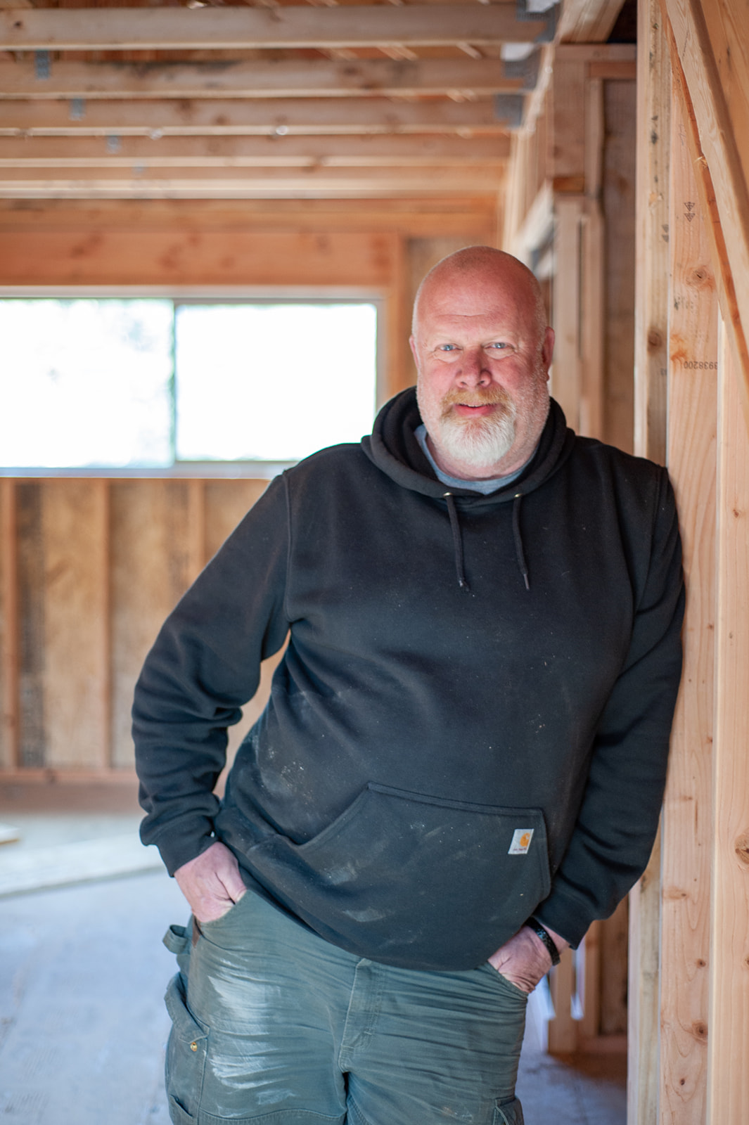 A man in a hoodie standing in a room with wood framing.