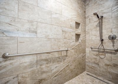 A beige tiled shower with a hand rail.