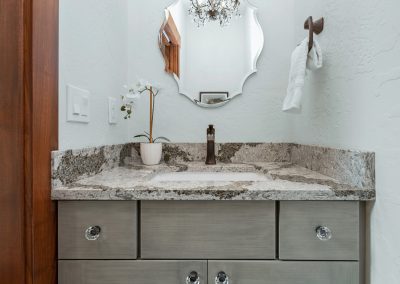 A bathroom with gray cabinets and a mirror.