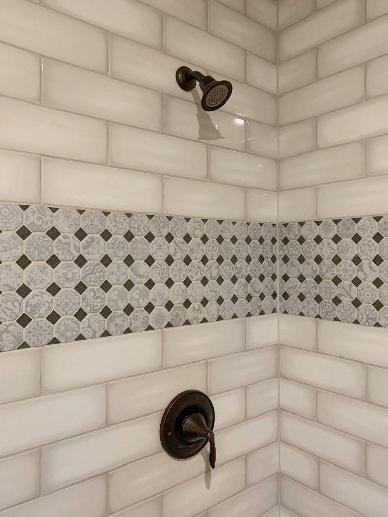 A white tiled shower with a black shower head.