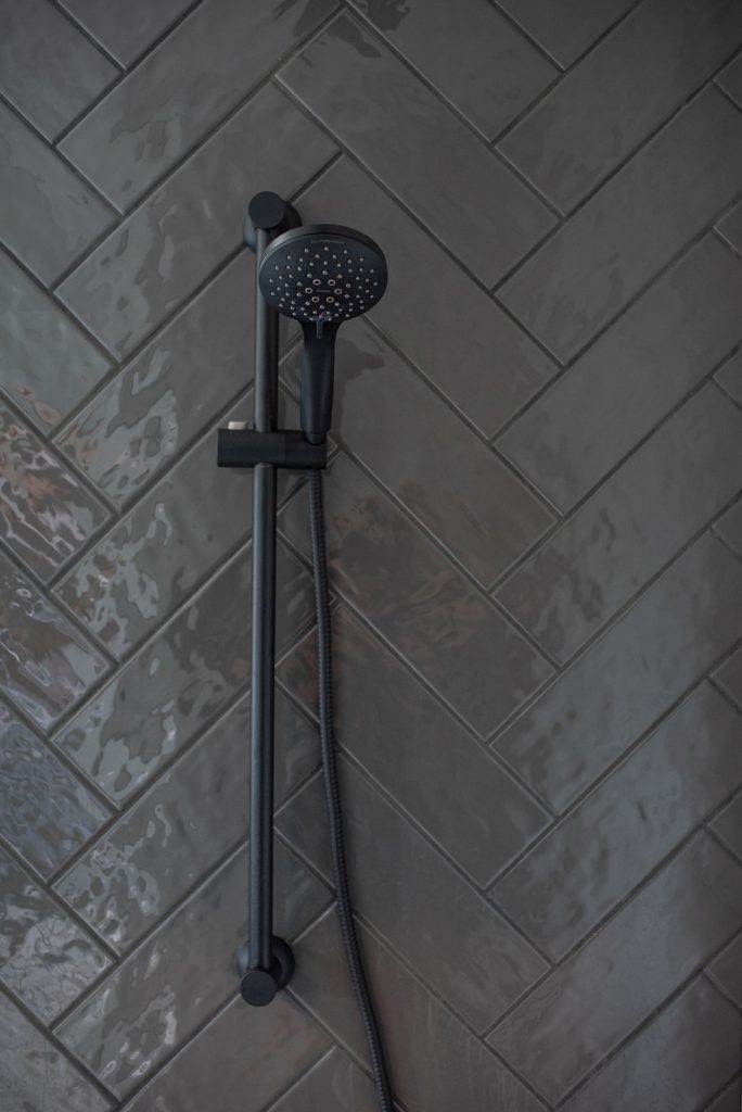 A black shower head on a tiled wall.