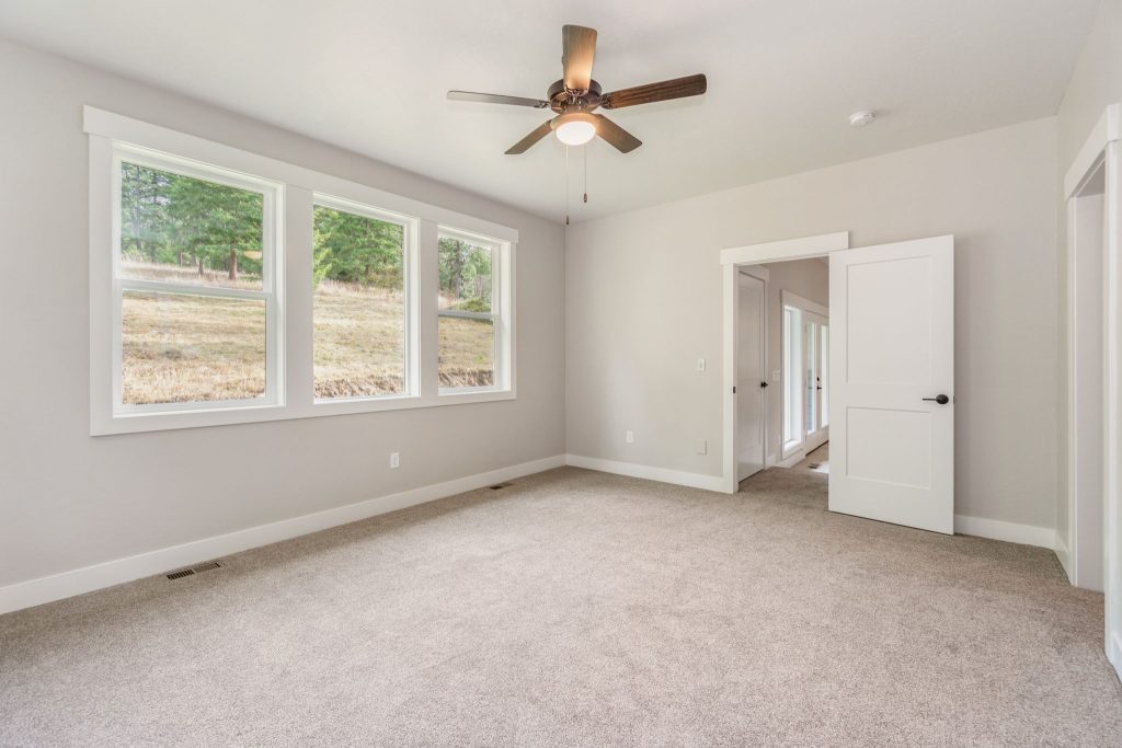 An empty room with a ceiling fan and windows.