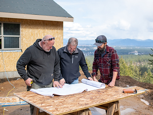 Three men standing around a table looking at blueprints.