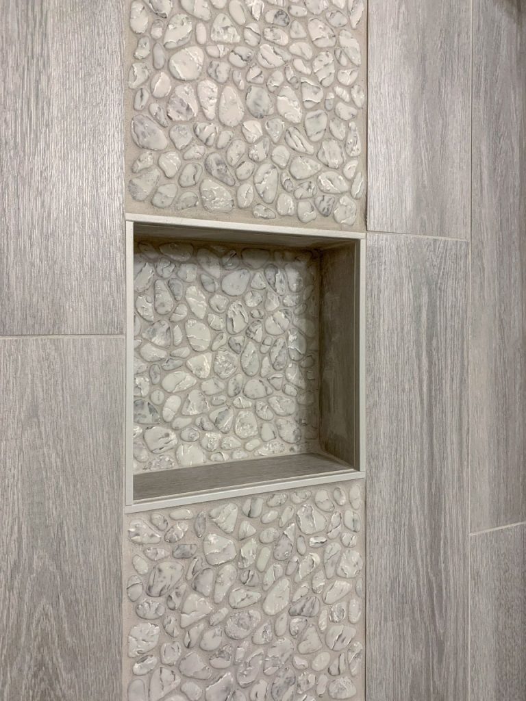 A shower with a tiled wall and a shelf.