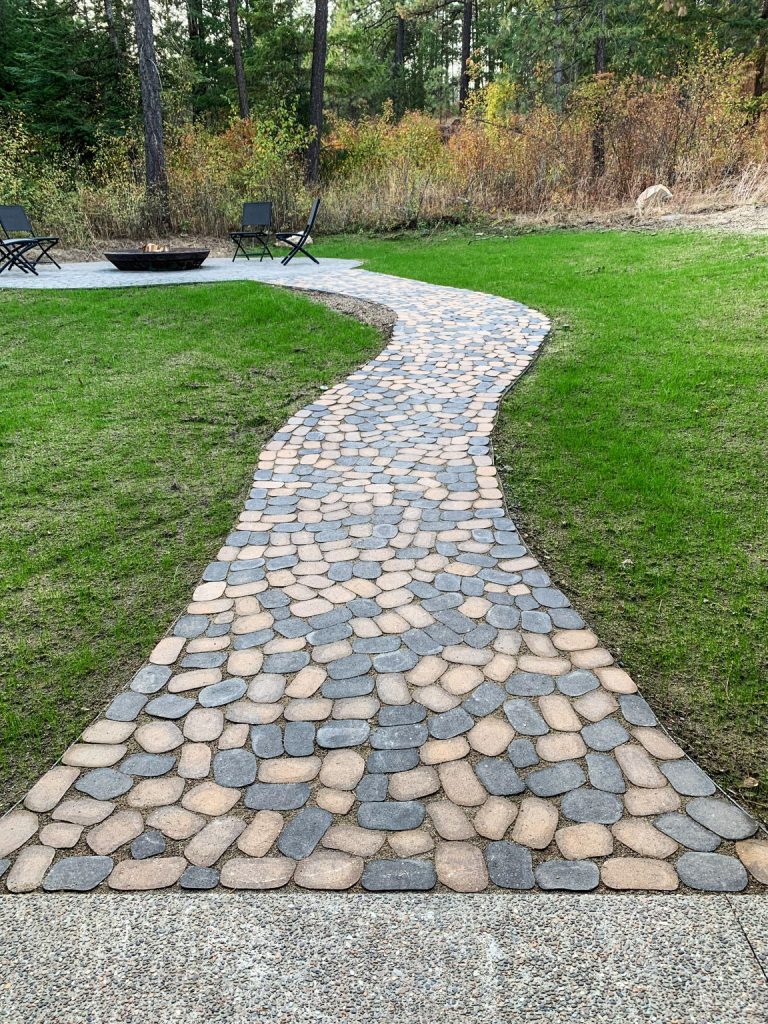 A stone walkway in a backyard with a fire pit.