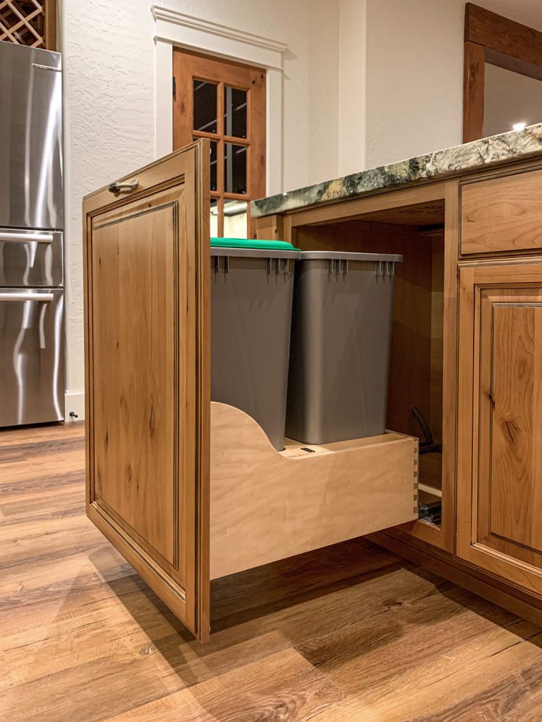 A kitchen with a trash can under a cabinet.