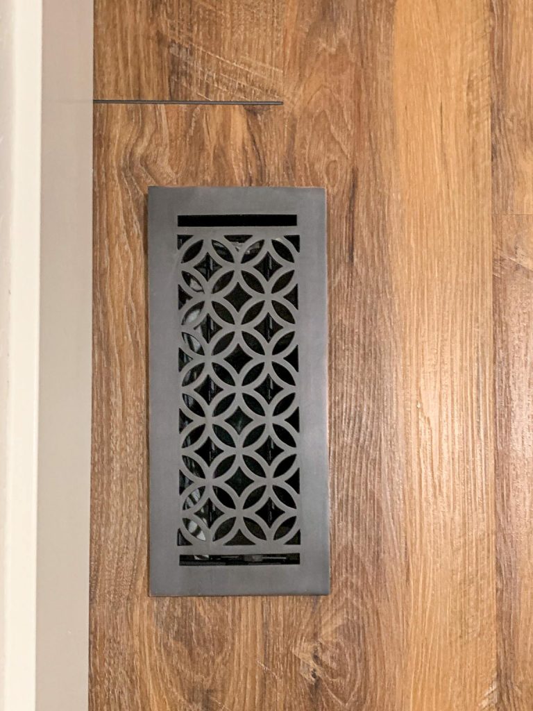 A decorative air duct grate on a wooden floor.