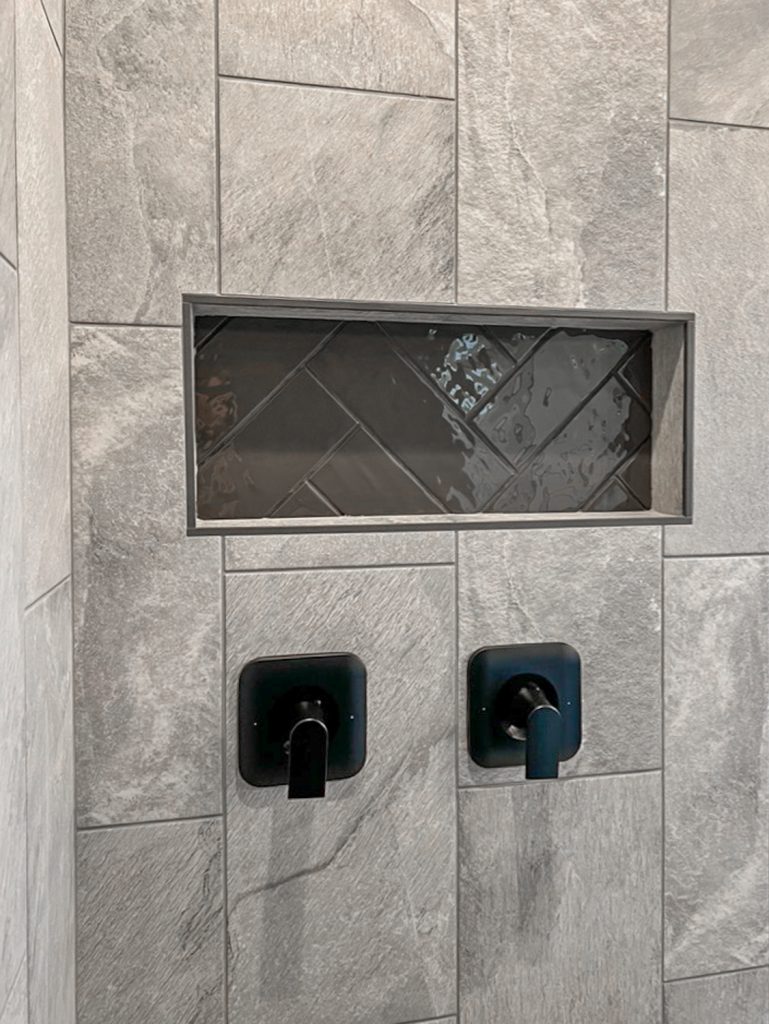A grey tiled shower with a black shower head.