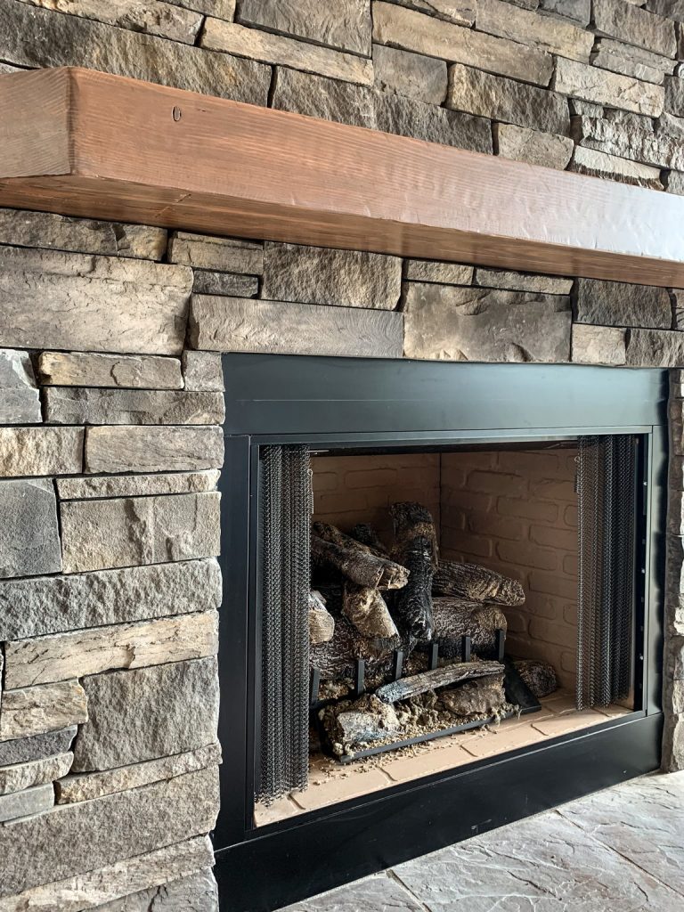 A stone fireplace with a wooden mantle and logs.