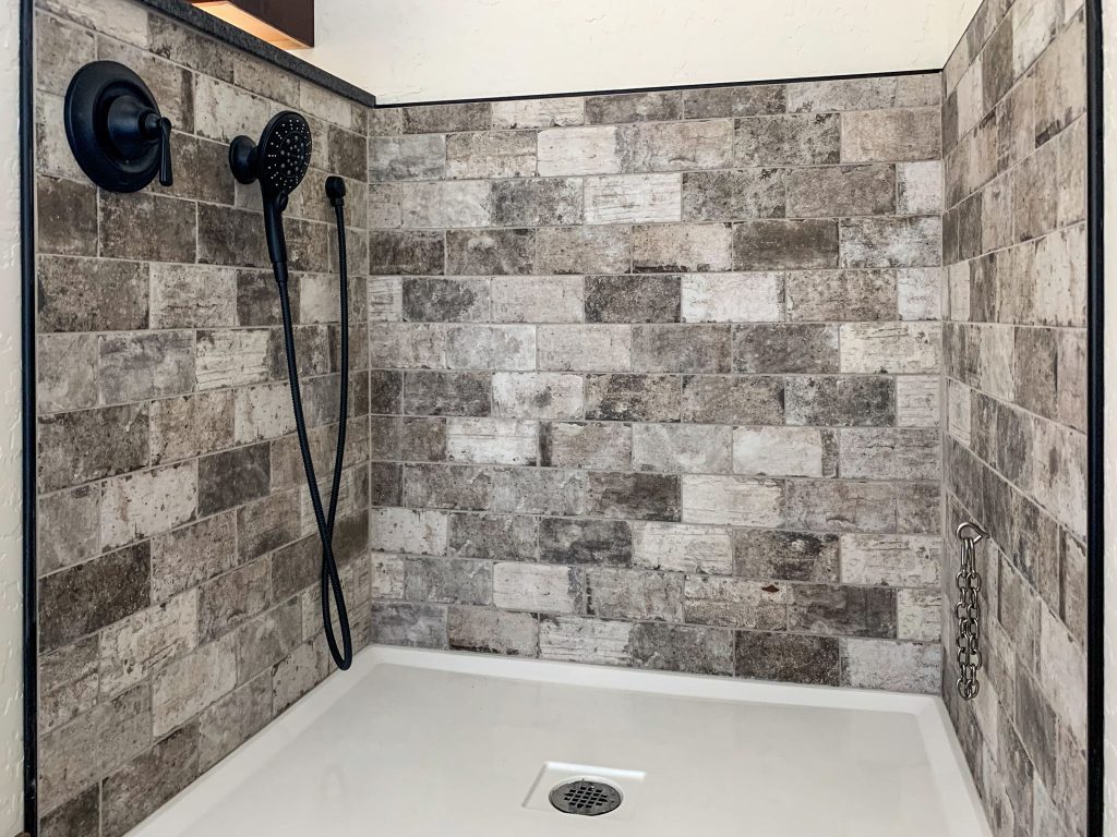A shower with tiled walls and a black shower head.