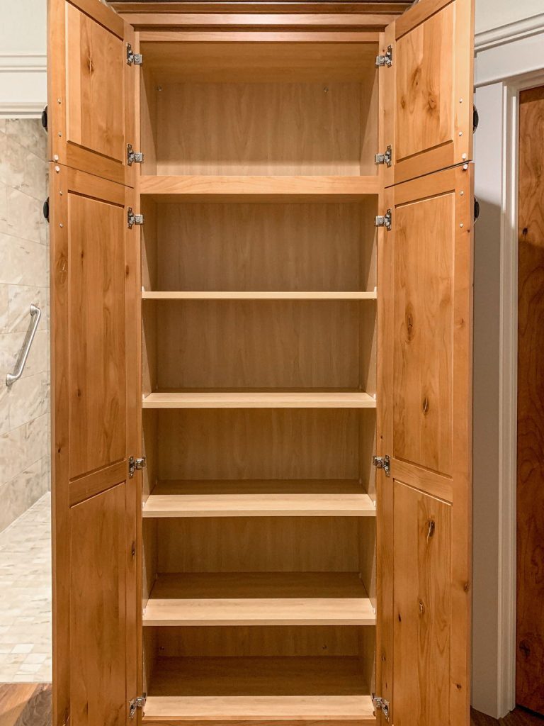 A wooden closet with doors open in a bathroom.