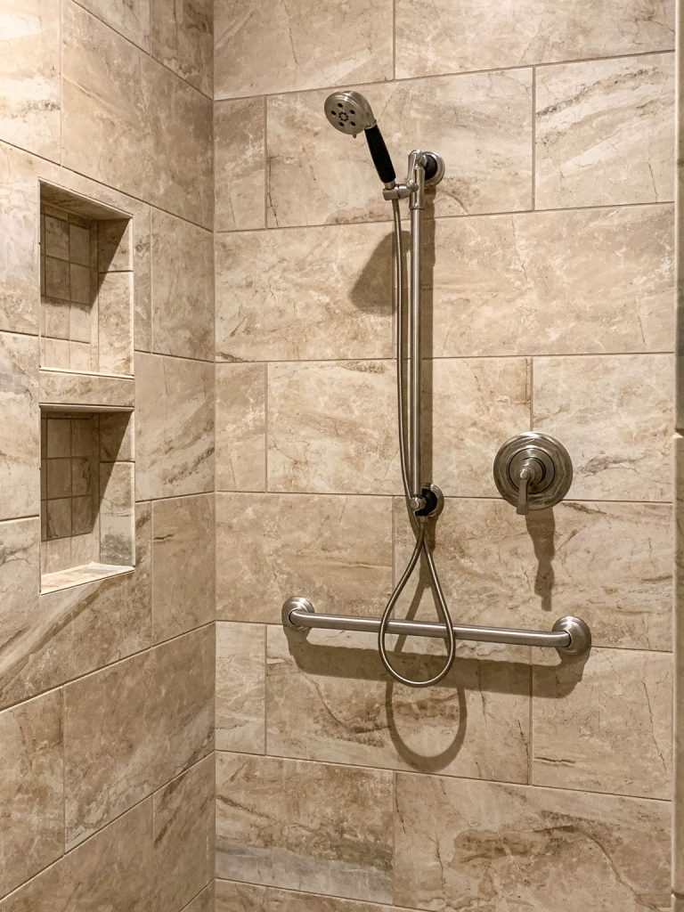 A beige tiled shower with a hand held shower head.