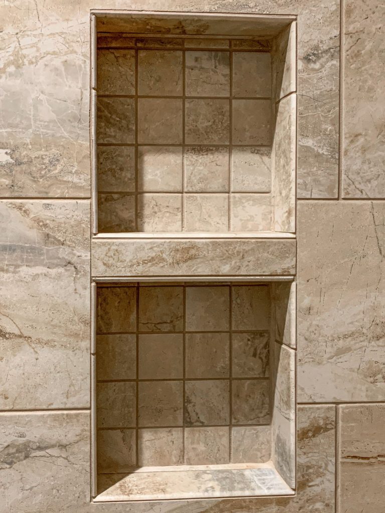 A tiled shower with two shelves in it.