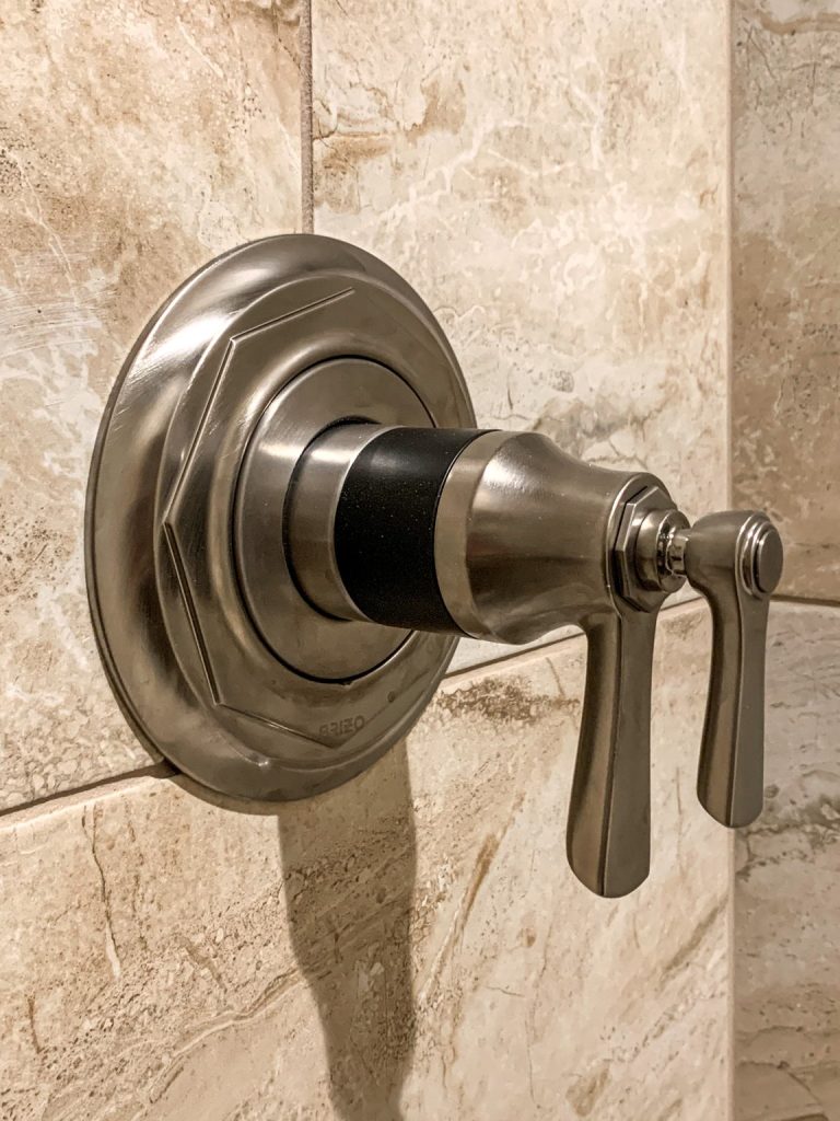 A shower faucet with a metal handle on a tiled wall.