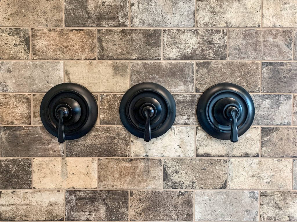 Three black faucets on a brick wall.