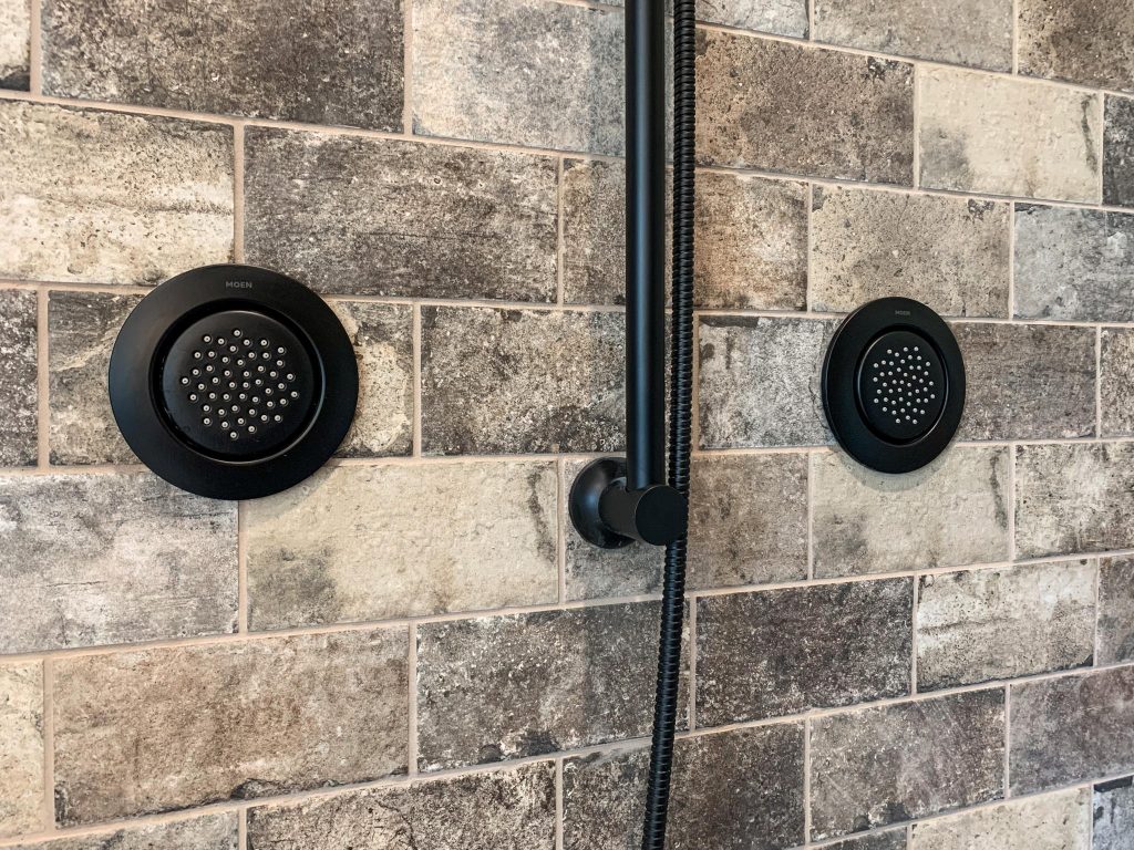 A black shower head and shower head on a tiled wall.