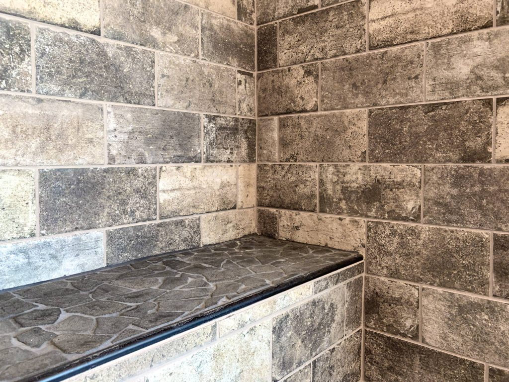 A shower with tiled walls and a bench.