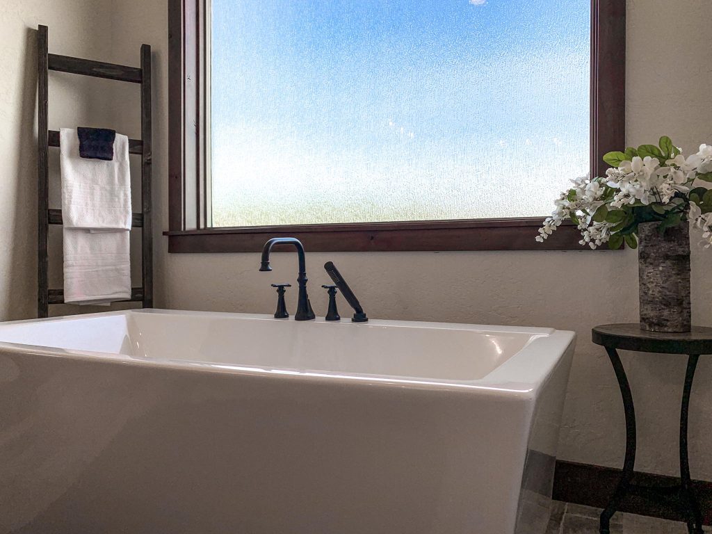 A white bathtub in a bathroom with a window.