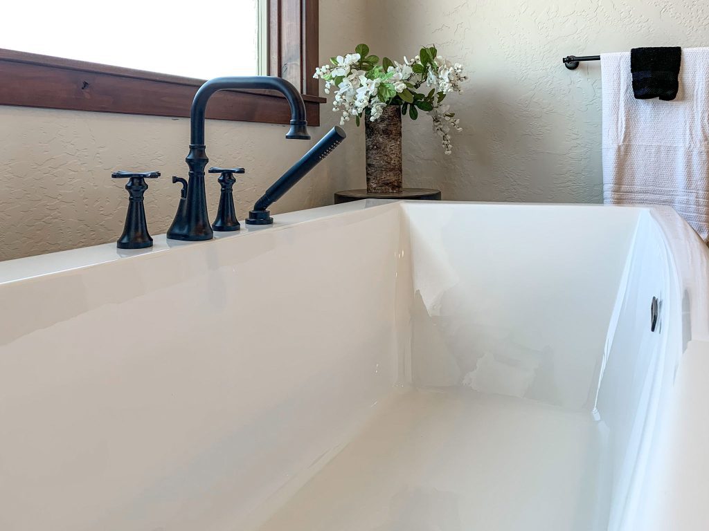 A white bathtub in a bathroom with black faucets.