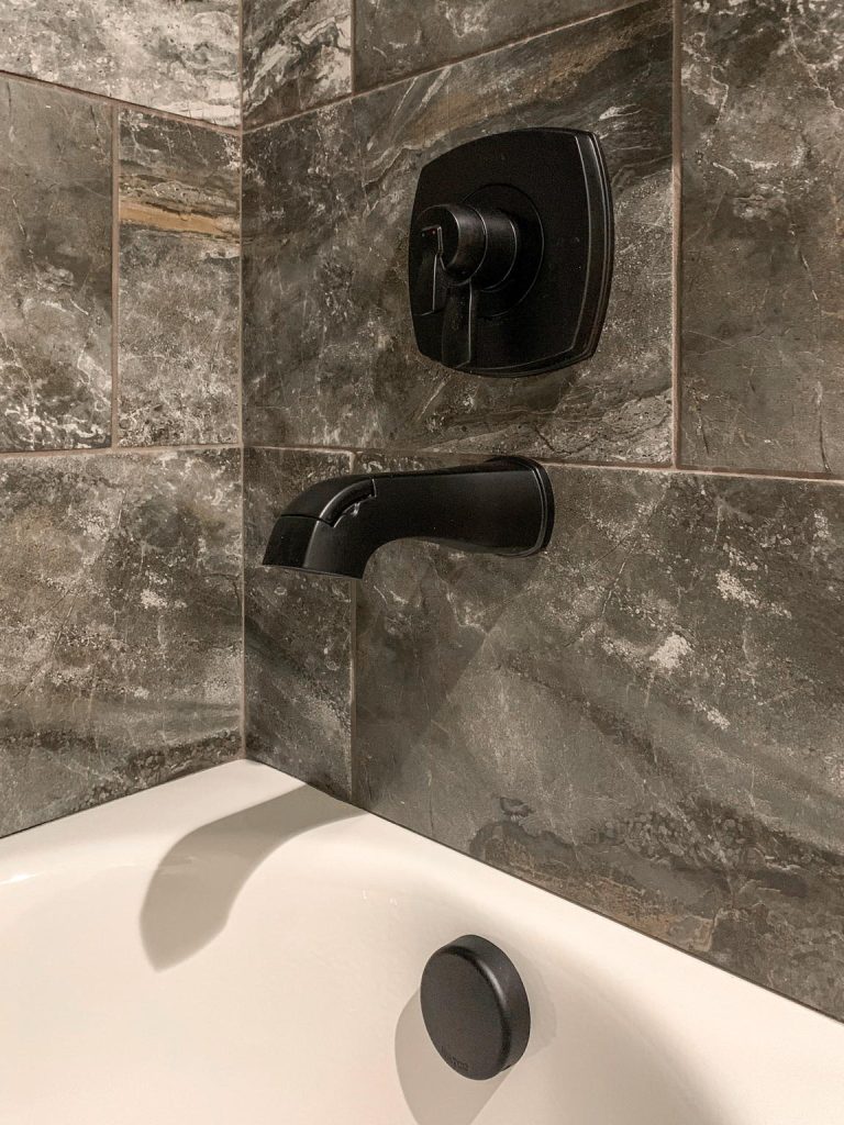 A bathroom with a black tiled wall and black faucet.