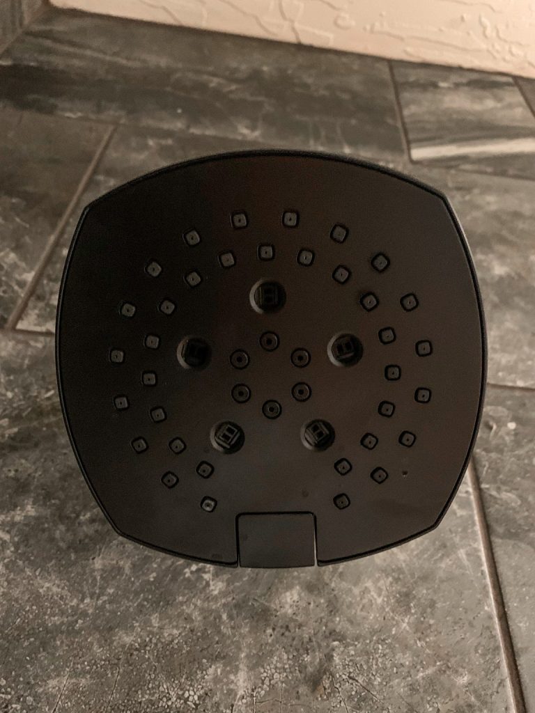 A black shower head sitting on a tile floor.