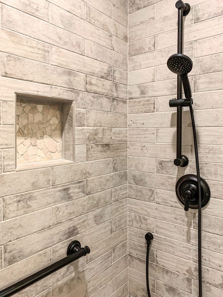 A white tiled shower with a black shower head.