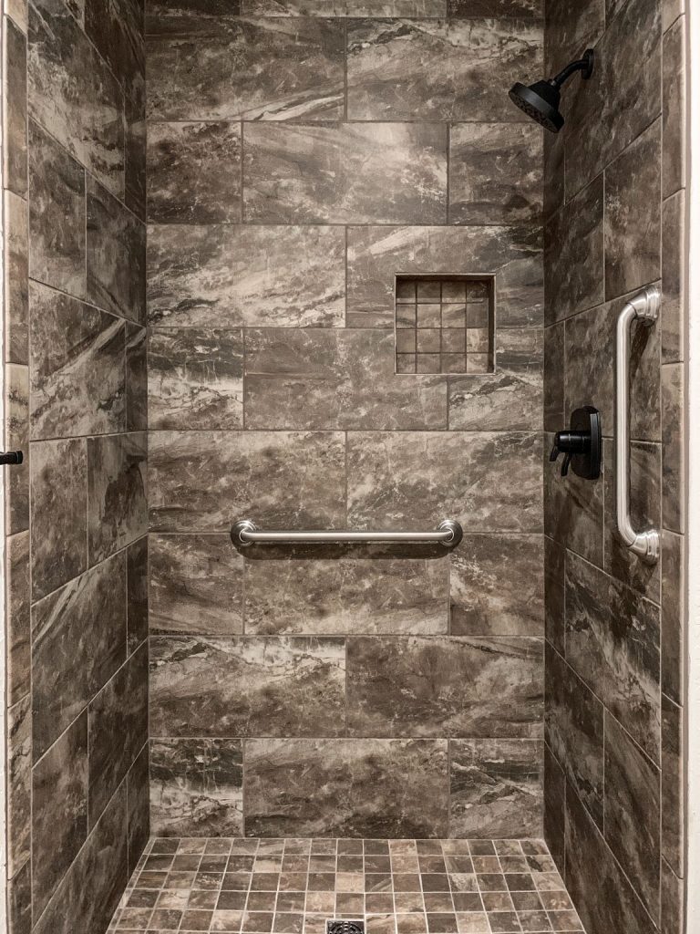 A walk in shower with brown tile and a handrail.