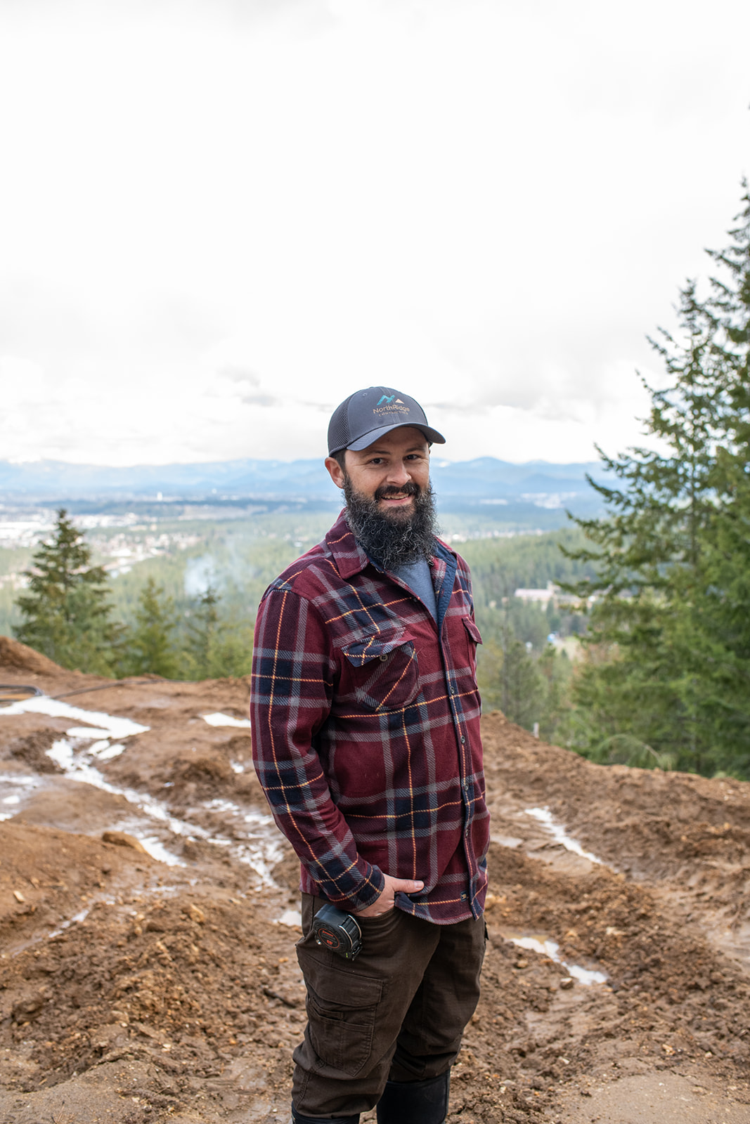 A bearded man in a plaid shirt standing on top of a hill.