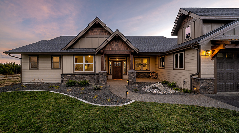 a wide shot of the Eaglecrest home's backyard, including a beautiful firepit and a brown, rustic angled home on a hill with pine forest mountains in the background